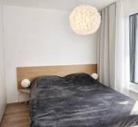 A bedroom in a one-room apartment with a bed, a lamp, and a wooden decor floor.