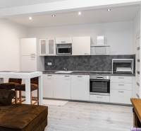 A modern kitchen in a studio apartment with white furniture and a wooden decor floor.