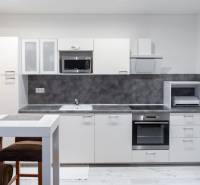 A kitchen with white cabinets, a bar table, and a wood-patterned floor in a studio apartment.