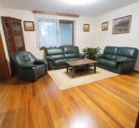 Living room in a family house with leather furniture and wood-patterned flooring.