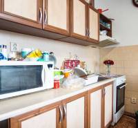 A kitchen with a microwave, a gas stove, and wooden cabinets in a two-room apartment.