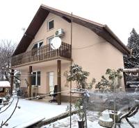 A family house covered in snow in Trnava with a wooden balcony and a garden.