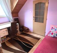 Children's room in the attic of a family house with a table, bed, and carpet.
