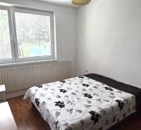 Bedroom with a bed and floral blanket, wooden decor floor, large window.