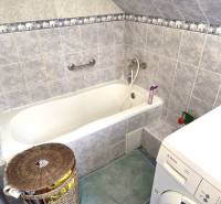 A bathroom with a bathtub, washing machine, and blue-white tiles in a family house.