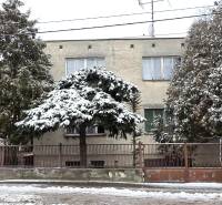 A family house in Trnava covered with snow, surrounded by trees, opposite apartment buildings.