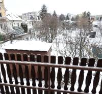 Snow-covered gardens and family houses in Trnava viewed through a wooden fence.