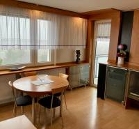 A dining room with wooden decor and windows in a 3-room apartment, overlooking greenery.