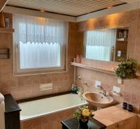 A bathroom in a 3-room apartment with a bathtub, subtly decorated tiles, and a mirror.