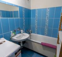 A bathroom in a 2-room apartment with blue tiles, a bathtub, and a washing machine.