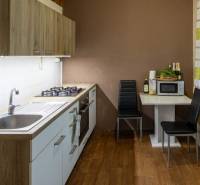 The kitchen of a two-room apartment with a wooden-patterned floor and a dining area.