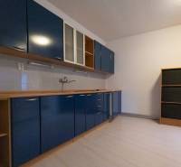 A kitchen in a 4-room apartment with cabinets, white tiles, and a wooden decor floor.