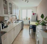 A kitchen in a 3-room apartment with light white cabinets and a dining table.