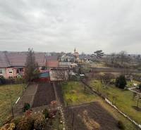 The view from Ludanice to gardens, houses, and a distant tower.