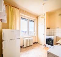 A kitchen in a 2-room apartment with a gas stove, a white refrigerator, and a window.