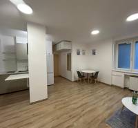 Studio apartment with a kitchenette, table, floor lamp with wooden decor, large window.