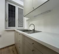 A kitchenette in a studio apartment with white cabinets and a wood-patterned floor.
