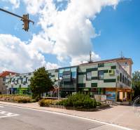 Building on Popradská Street in Stará Ľubovňa with blue sky, flowers, and a sidewalk.