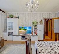 Living room with a sofa, cabinets, a table, and a television in a three-room apartment with a wooden decor floor.