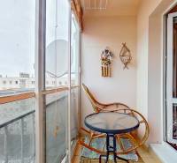 A balcony in a 3-room apartment with rattan chairs and a table, view of apartment buildings.