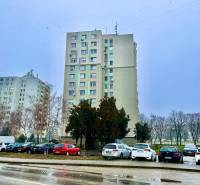 In Nové Zámky on S.H. Vajanský Street, there are tall buildings and parked cars.