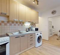 A kitchen in a 2-room apartment with beige cabinets, appliances, and a wooden decor floor.