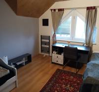 A room in a family house with a wooden decor floor, a desk, a bed, and a carpet.