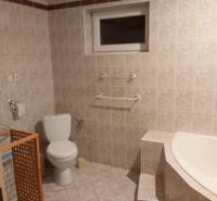 A bathroom in a family house with a bathtub, toilet, and tiles in neutral tones.