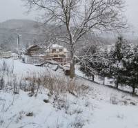 A snowy landscape in Orovnica, with a family house and trees in the background.