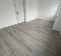 A room in a 2-bedroom apartment with a wood-patterned floor and white walls.