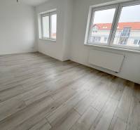 A bright room with wood-patterned flooring and large windows in a 2-room apartment.