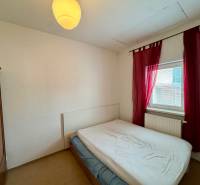 Bedroom in a 2-room apartment with a wooden wardrobe and a window with red curtains.