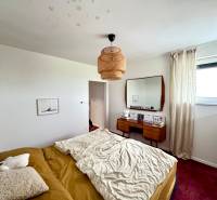 A bedroom in a family house with a bed, a mirror, and a red carpet on the floor.
