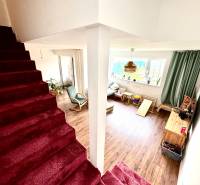 Interior of a family house with a staircase and a living room with a wood-patterned floor.