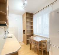 A kitchen in a 2-room apartment with a wooden decor floor, simple furniture, and appliances.
