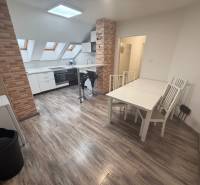 Interior of a one-room apartment with a wooden decor floor and a kitchen with brick cladding.