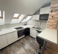 A kitchen area in a studio apartment with a wooden decor floor and skylights.