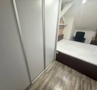 A bedroom in a studio apartment with a wood-patterned floor and a built-in wardrobe.