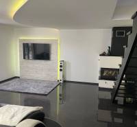 Living room in a family house with a staircase, fireplace, and television on the wall.