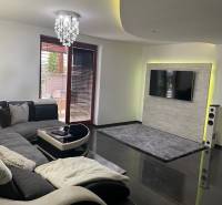 Living room in a family house with a sofa and a television on a wall with stone cladding.