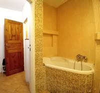 A bathroom in a family house with a bathtub clad in stone tiles and wooden doors.