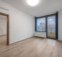 A room with a wooden decor floor, a window, and glass doors in a two-room apartment.