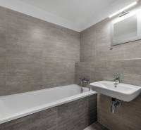 A bathroom in a 2-room apartment with a bathtub, sink, and gray tiles.