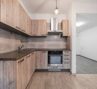 A kitchen in a 2-room apartment with a wooden decor floor, light cabinets, and appliances.