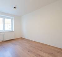 A bright room with a wood-patterned floor in a three-room apartment with a light above the window.