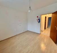 A room with a wooden decor floor in a 3-room apartment, light wall, open door.