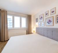 A bright bedroom with wood-patterned flooring, a bed, and wall pictures in a two-room apartment.