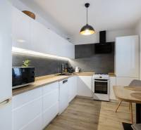 A kitchen in a 2-room apartment with white cabinets and a wooden decor floor.