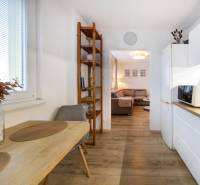 A kitchen in a 2-room apartment with a dining table, a shelf, and a floor with a wood decor.