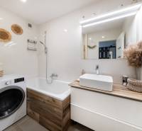 A bathroom in a 2-room apartment with a washing machine and a bathtub, bright tiles and decorations.